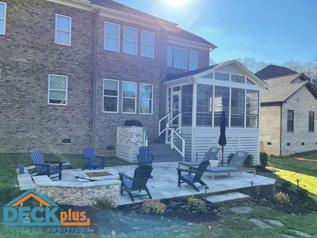 Screened-porch with Keystone patio behind a two-story brick home. Built-in stone firepit and navy blue Adirondack chairs on patio.